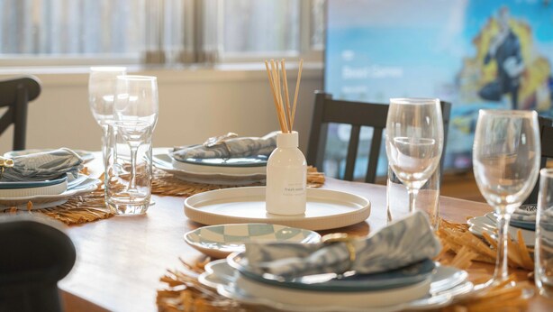 A dining table set with plates, glasses, and a bottle of fresh ocean water. - Soothing 4-bedroom house with AC in Yarrabilba (Yarrabilba)