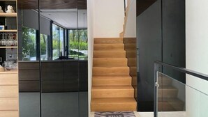 A modern interior with a wooden staircase, a glass railing, and a view of greenery outside. - Joy Villa Phu Quoc (Phu Quoc Island)