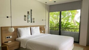 A modern bedroom with a large bed, bedside tables, a nightstand, and a view of greenery through a large window. - Joy Villa Phu Quoc (Phu Quoc Island)