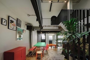 A room with a staircase, a dining area with a green table and orange chairs, and a red cabinet.