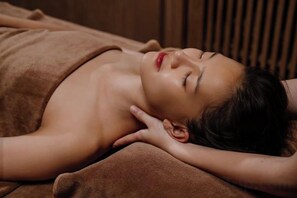 A person lying on a bed with a brown blanket, in a room with wooden paneling.