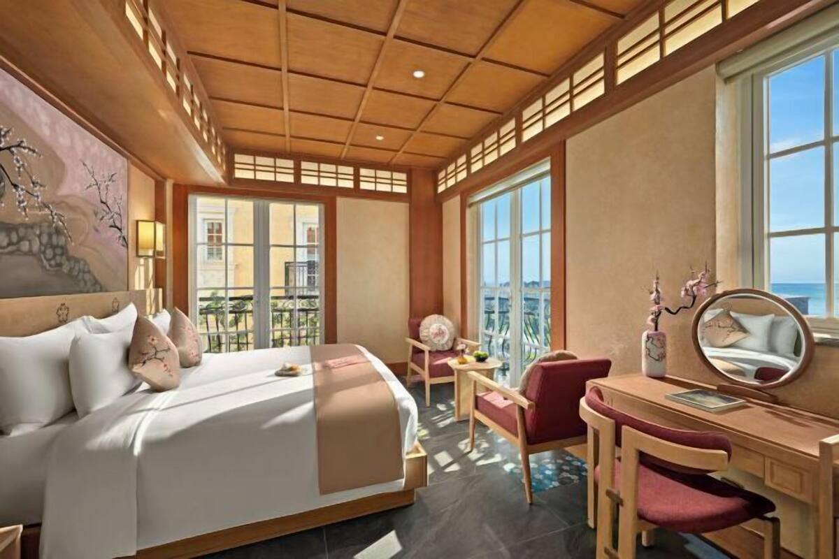 Ein Hotelzimmer mit Bett, Schreibtisch, Stuhl, einem großen Fenster und Ausblick nach außen.