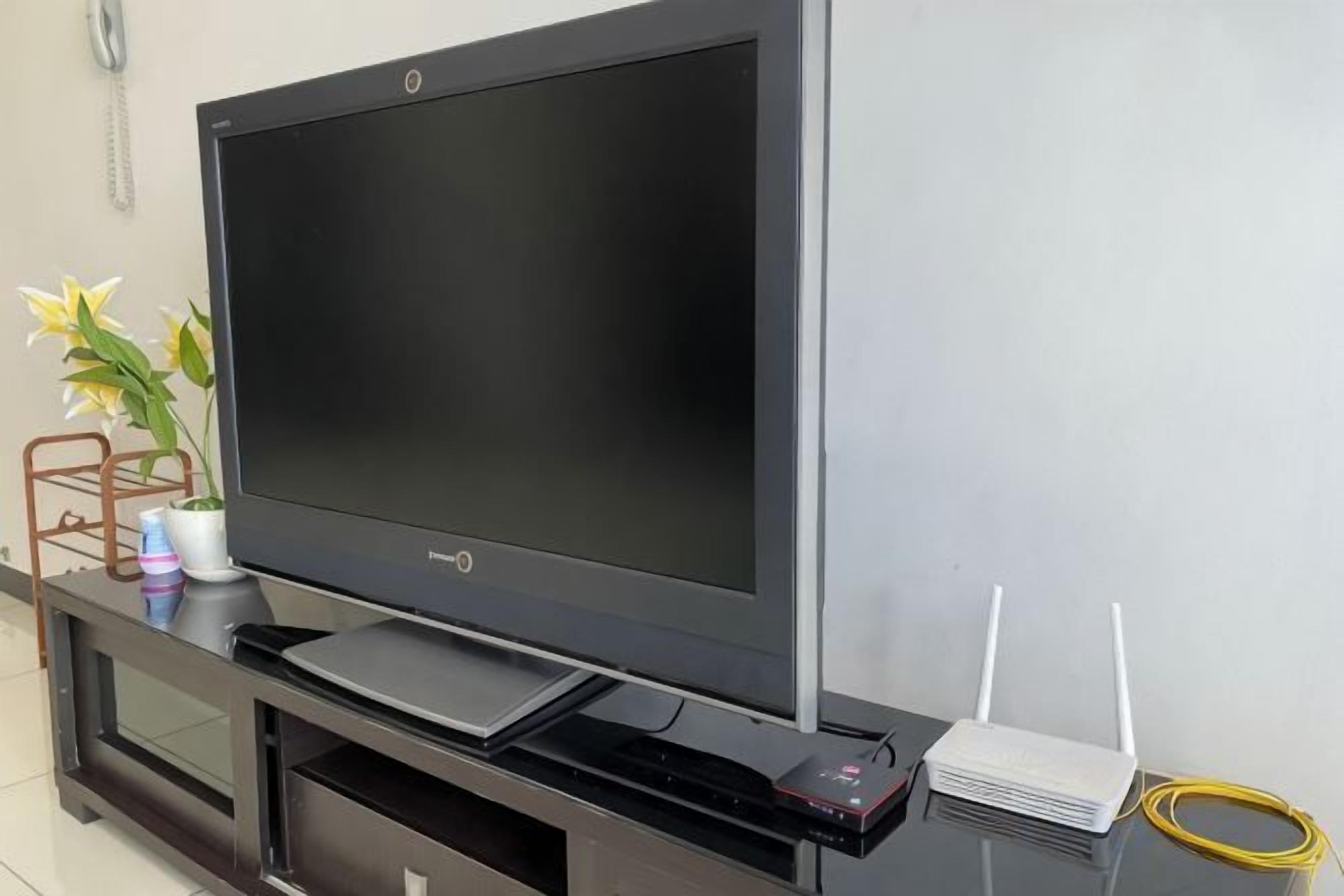 Een flatscreen televisie op een zwarte entertainmentkast, met een witte router en een gele kabel.