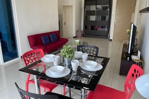 A dining area with a glass table, red and black chairs, white plates, and a red sofa in the background.