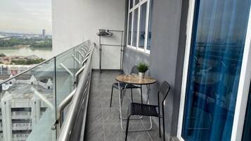Un balcón con una mesa y sillas, una planta en maceta y vistas de un río y edificios.