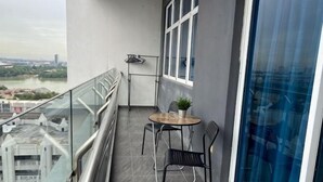 Un balcone con tavolo e sedie, una pianta in vaso e vista su un fiume ed edifici.