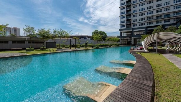 Una piscina con bordo in legno, circondata da un'area verde e un edificio moderno a più piani.