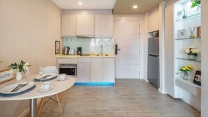 A compact kitchen with white cabinets, a dining table set for two, and a refrigerator. - Seven Seas Condo Resort OB D7 (Pattaya)
