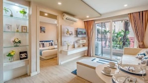 A modern living room with a sofa, a dining table set with plates and glasses, a TV mounted on the wall, and a balcony with plants. - Seven Seas Condo Resort OB D7 (Pattaya)