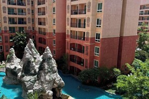 Un hotel su più piani con balconi, una zona piscina con formazioni rocciose e una vegetazione rigogliosa.