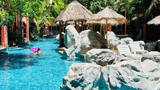 A swimming pool with large rocks, lounge chairs, and thatched umbrellas. - Seven Seas Condo Resort OB D7 (Pattaya)