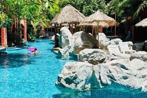 Una piscina con grandi rocce, lettini e ombrelloni di paglia.
