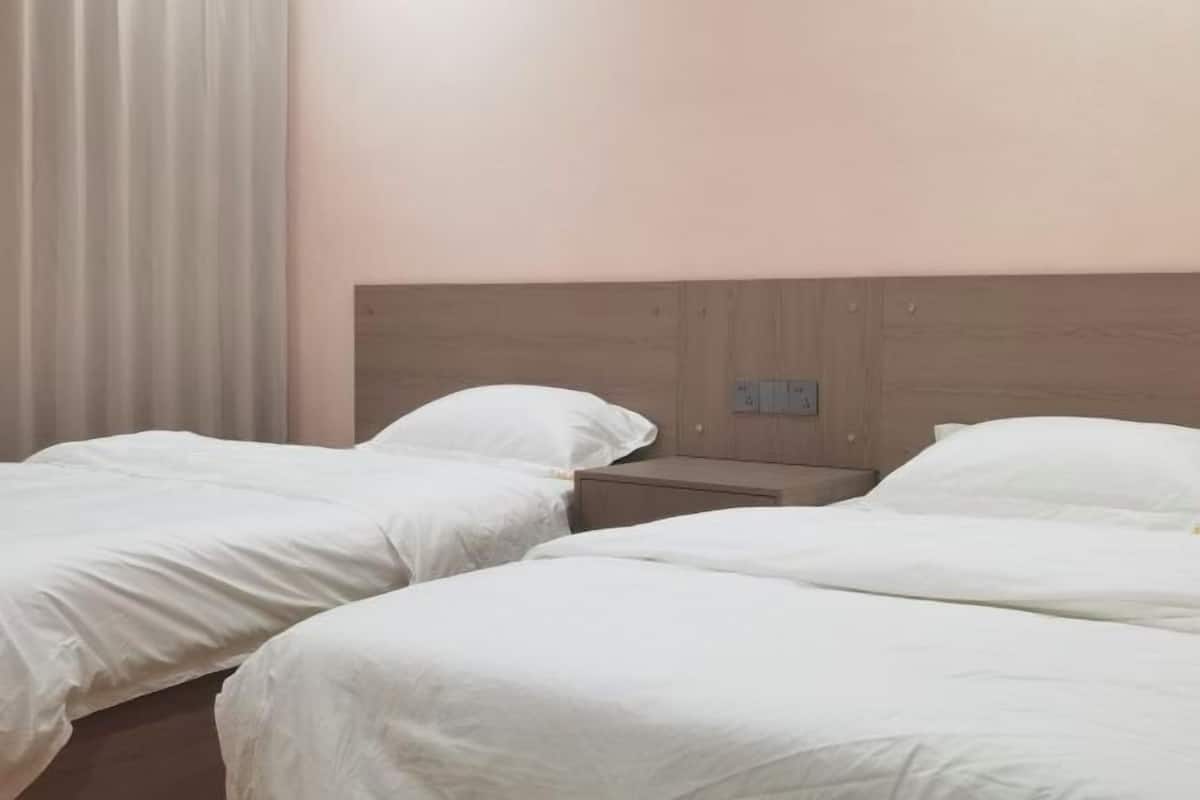 A hotel room with two single beds, a wooden headboard, a nightstand, and a wall socket.