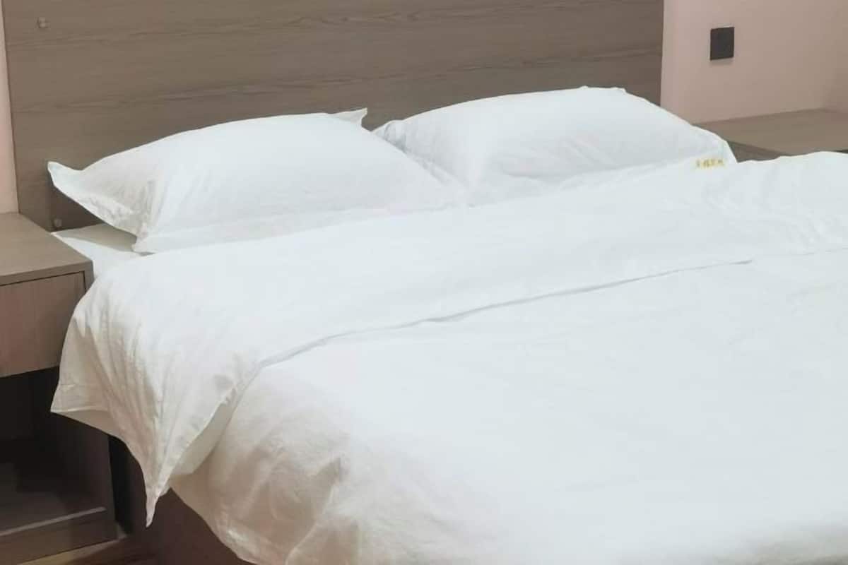 A neatly made bed with white bedding and pillows, a wooden headboard, and a nightstand with a lamp.