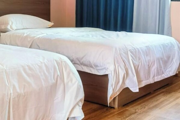 Ein Zimmer mit zwei Betten, Holzböden und einem Fenster mit Vorhängen.