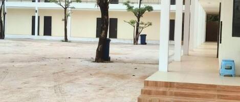 A courtyard with a building featuring a covered walkway, trees, and a blue stool.