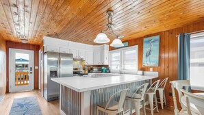 A modern kitchen with wooden ceiling, white cabinets, stainless steel appliances, and a central island with bar stools. - Hot Tub-Waterfront 4BD Home-Cherry Grove-Pet Friendly-Sleeps 14 (North Myrtle Beach)