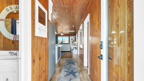 A hallway with wooden walls, a starfish-patterned rug, and a view into a kitchen area. - Hot Tub-Waterfront 4BD Home-Cherry Grove-Pet Friendly-Sleeps 14 (North Myrtle Beach)