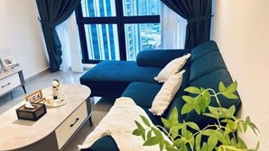 Een moderne woonkamer met een donkergroene bank, een klein tafeltje met zakdoos en dienblad, en uitzicht op hoge gebouwen door grote ramen.