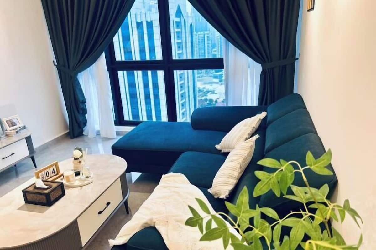 Een moderne woonkamer met een donkergroene bank, een klein tafeltje met zakdoos en dienblad, en uitzicht op hoge gebouwen door grote ramen.