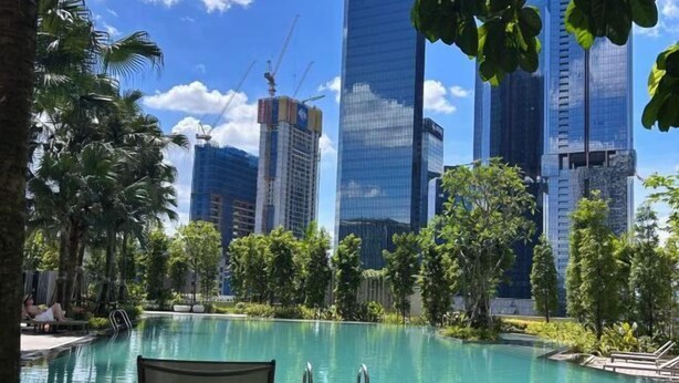 Zwembadterras met uitzicht op hoge gebouwen, omringd door groen en palmbomen.