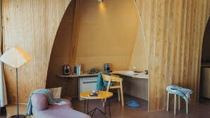 A cozy room with a curved wooden wall, a round table, a cushioned seating area, a desk with a chair, and a standing lamp. - SANU 2nd Home Kawaguchiko1st (Narusawa)