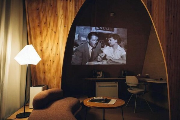Une pièce chaleureuse avec un mur en bois, un grand écran, un canapé, une petite table et une lampe.