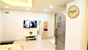A modern living room with a flat-screen TV, a wooden shelf, a refrigerator, and a clock on the wall. - Seoul Dajeong House/Hongdae Entrance Sta.Exit7. Party room. Lovely Big House (Seoul)