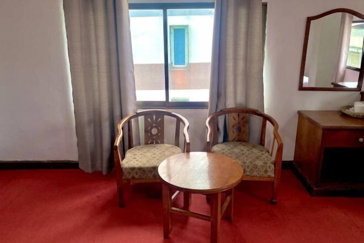 A room with two wooden chairs, a small round table, a wooden cabinet, and a window with curtains.