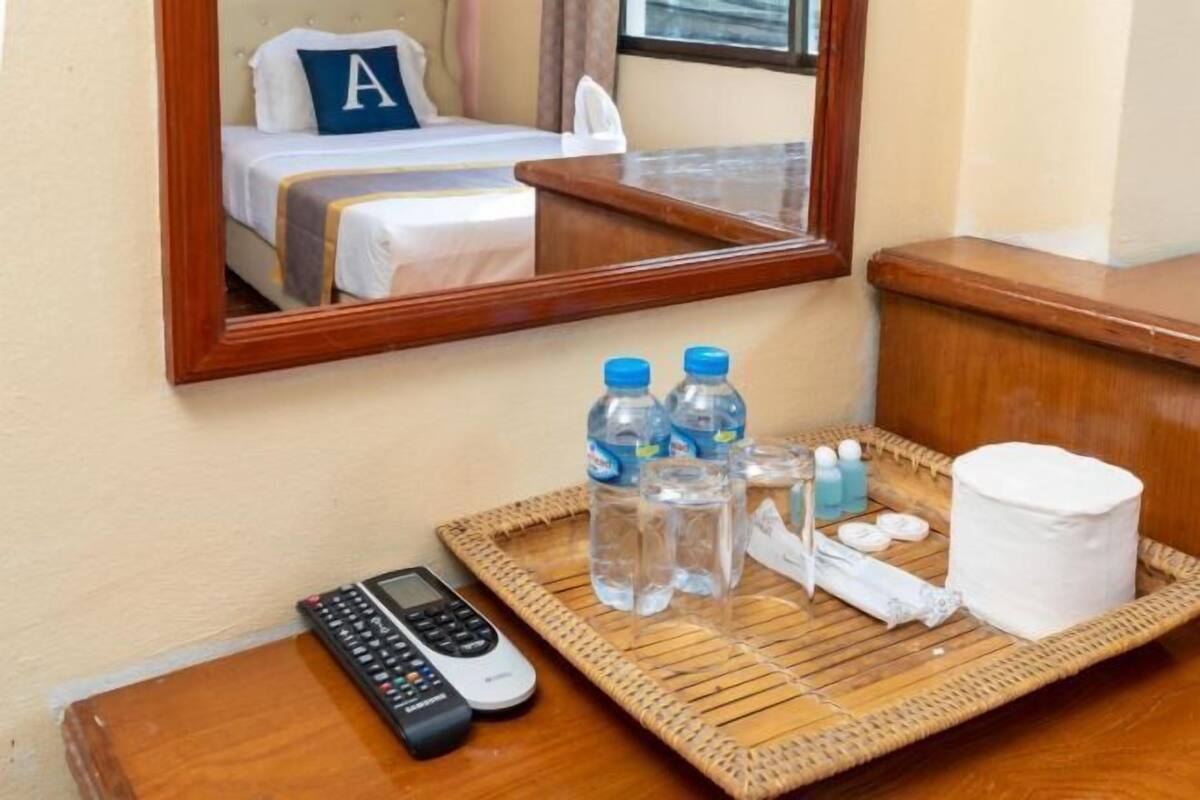 A hotel room with a bed, a mirror, a tray with toiletries, and a remote control.