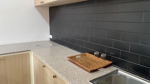 A kitchen with light wood cabinets, a granite countertop, and black tiled backsplash. - Anou Hotel (Vientiane)