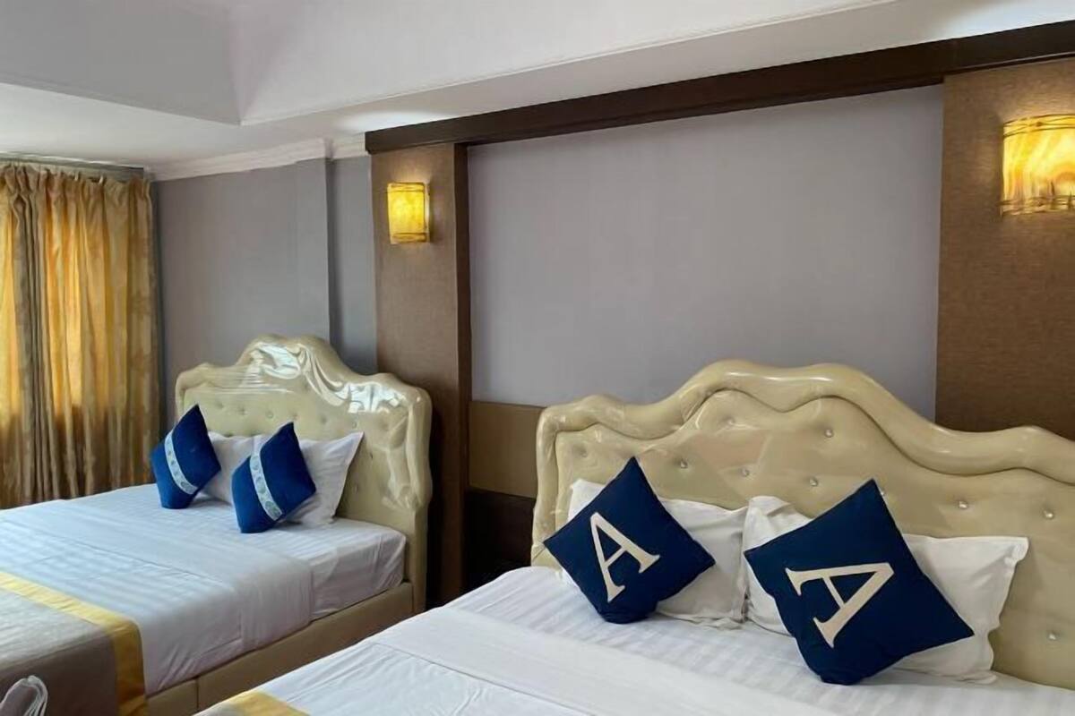 A hotel room with two beds, each with a headboard and pillows, and a large window with curtains.