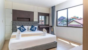 A modern hotel room with a large bed, a headboard with storage compartments, a bedside table, and a large window offering a city view. - Anou Hotel (Vientiane)