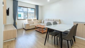 A modern living room with a sofa, a dining table with chairs, and a TV mounted on the wall. - Anou Hotel (Vientiane)