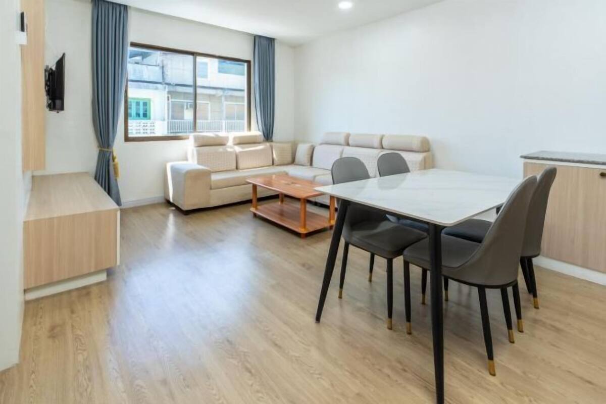 A modern living room with a sofa, a dining table with chairs, and a TV mounted on the wall.