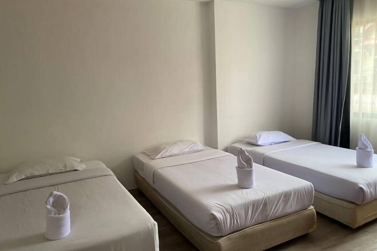 A hotel room with three single beds, each with a neatly folded towel and a pillow.