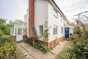 Une maison à deux étages avec une cheminée en briques, une façade blanche et une porte bleue.