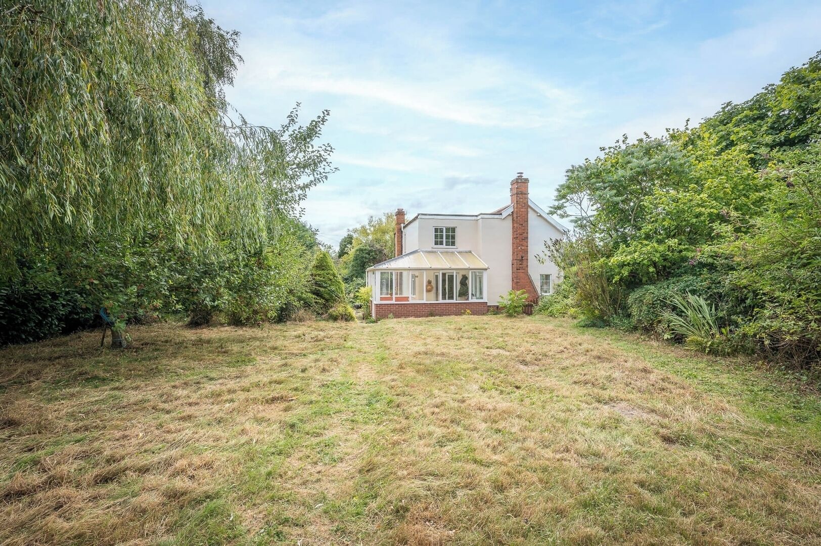 Een huis met een grote tuin, schoorsteen en een conservatorium.