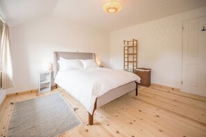 Une chambre à coucher comprenant un lit, une table de chevet, une commode, une lampe, une échelle en bois, un panier en osier, une porte et une fenêtre avec des rideaux.