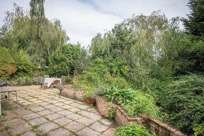 Une terrasse avec une table et des chaises, entourée d’une végétation luxuriante et d’arbres.