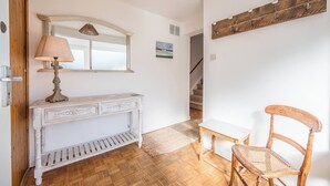 A hallway with a white console table, a lamp, a wooden chair, a mirror, and a staircase in the background.