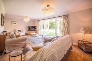A modern living room with a sofa, armchair, and TV, a coffee table, and a large window with curtains. - 5 Church Close (7 guests), Aldeburgh (Aldeburgh)