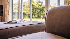 A cozy living room with a sofa, a window with curtains, and a pair of glasses on a book.