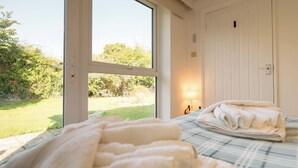 A bedroom with a large window, a bed with a plaid bedspread, and a neatly folded towel on the bed.