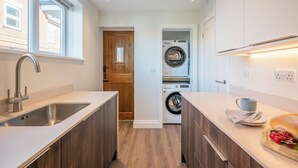 A compact kitchen with a sink, wooden cabinets, a window, and a washing machine in the background. - 1 Leiston Court, Leiston (Leiston)