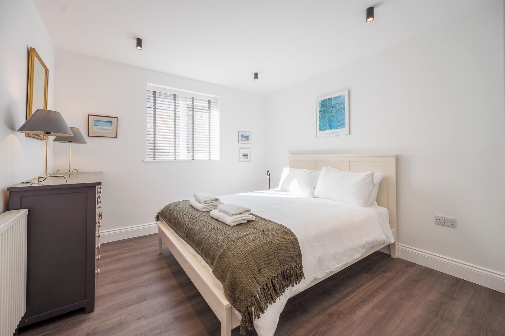 Quarto com cama, luminárias de cabeceira, cômoda e janela com persianas.