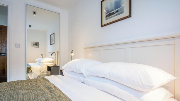 A neatly made bed with white linens, a bedside lamp, and a framed picture on the wall. - 1 Leiston Court, Leiston (Leiston)