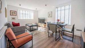A modern living room with a sofa, coffee table, and dining area. There is a television and a window with blinds. - 1 Leiston Court, Leiston (Leiston)