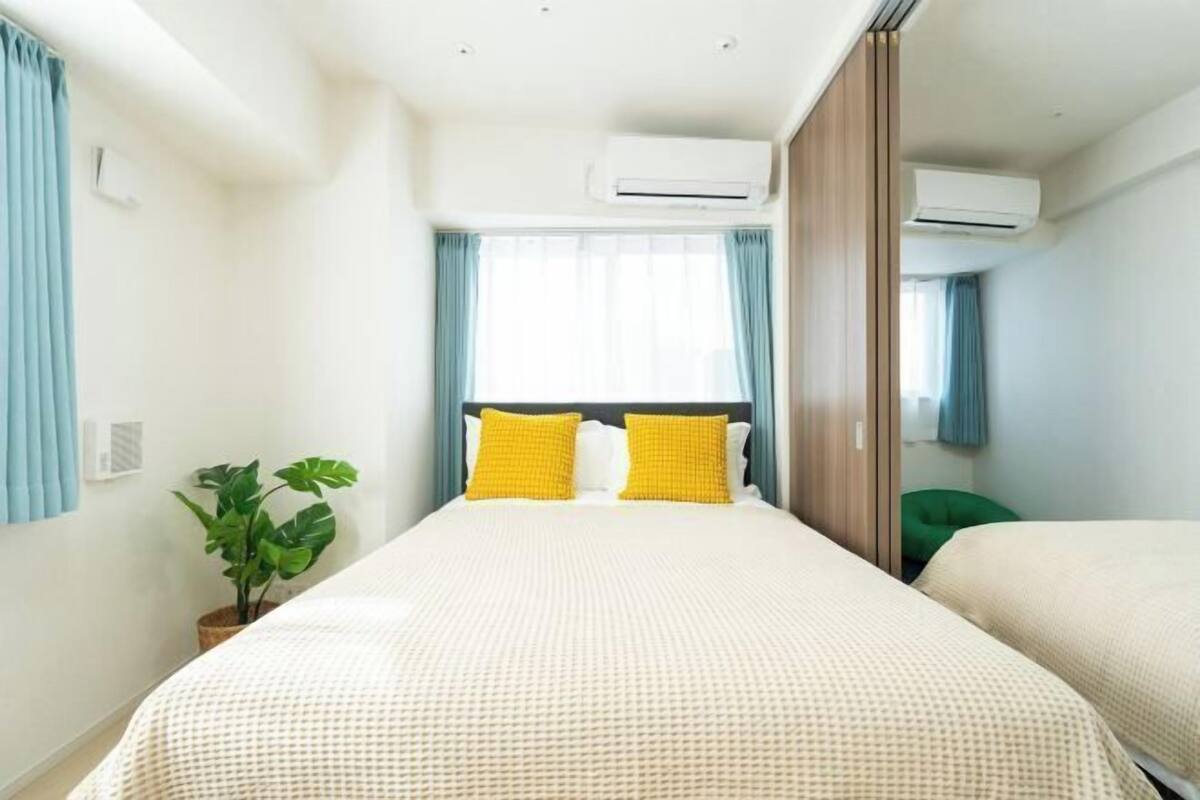 A hotel room with a large bed, two air conditioning units, a potted plant, and a green chair.