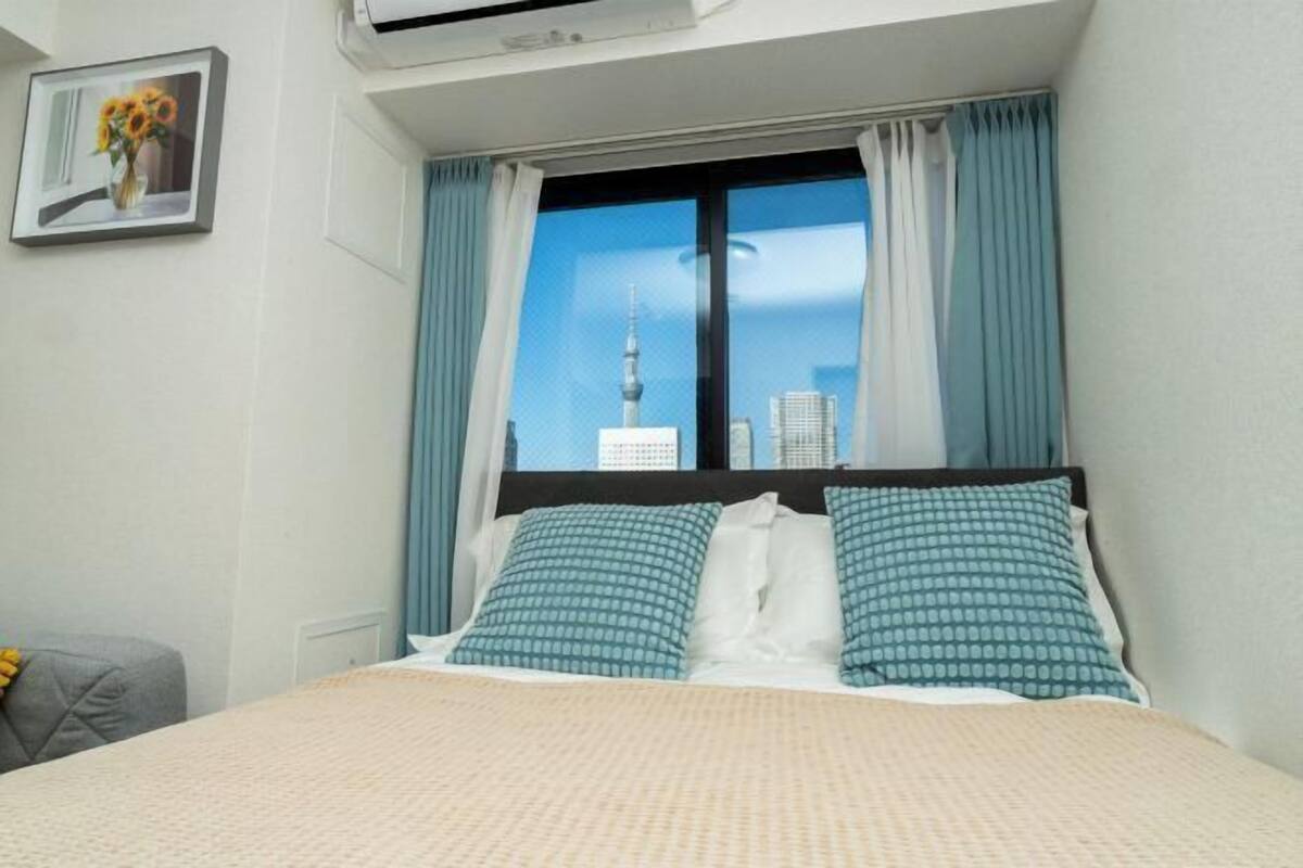 A hotel room with a bed, a window with curtains, a framed picture on the wall, and a view of a tower.
